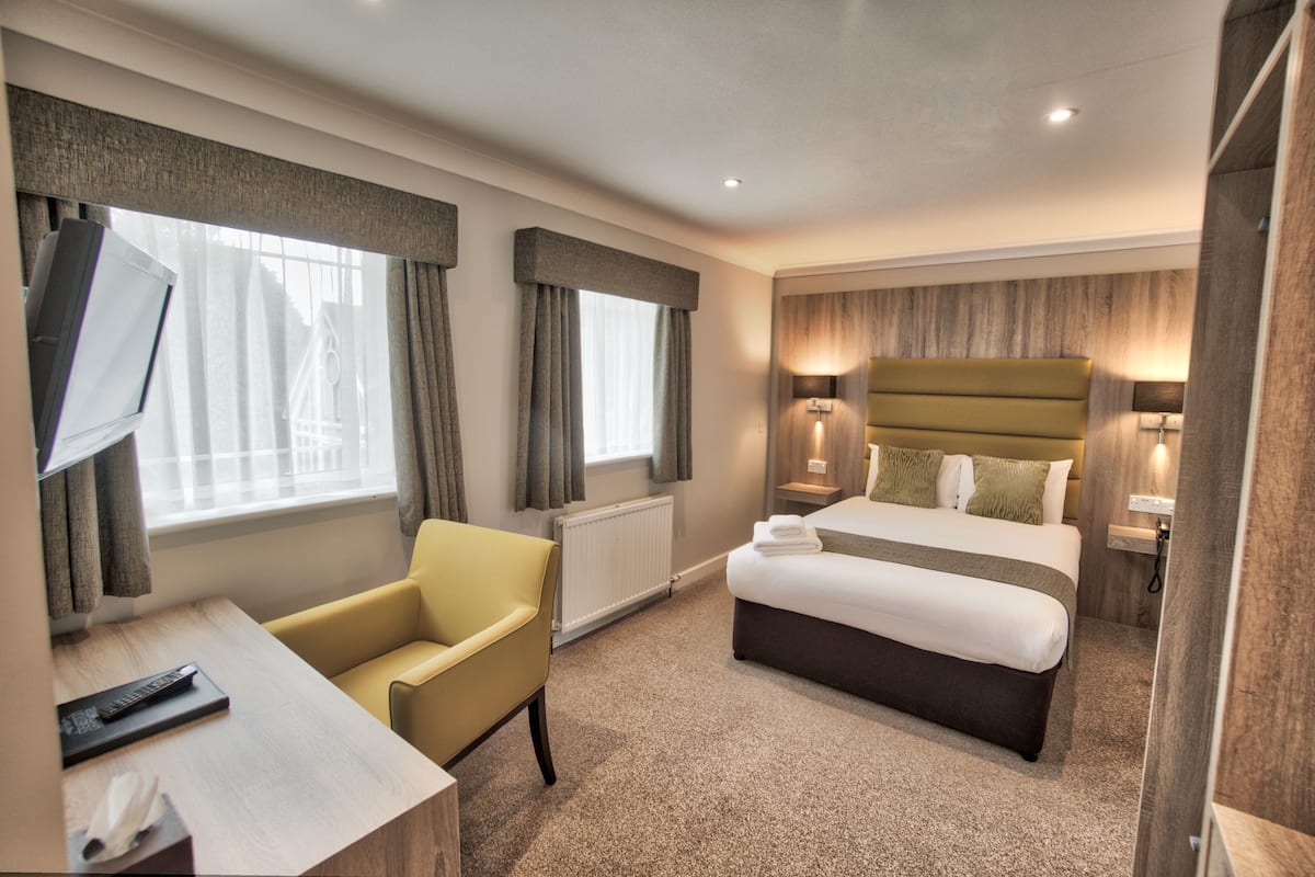 Ein Hotelzimmer mit einem Bett, einem Schreibtisch, einem Sessel, einem Fernseher und einem Fenster mit Vorhängen.