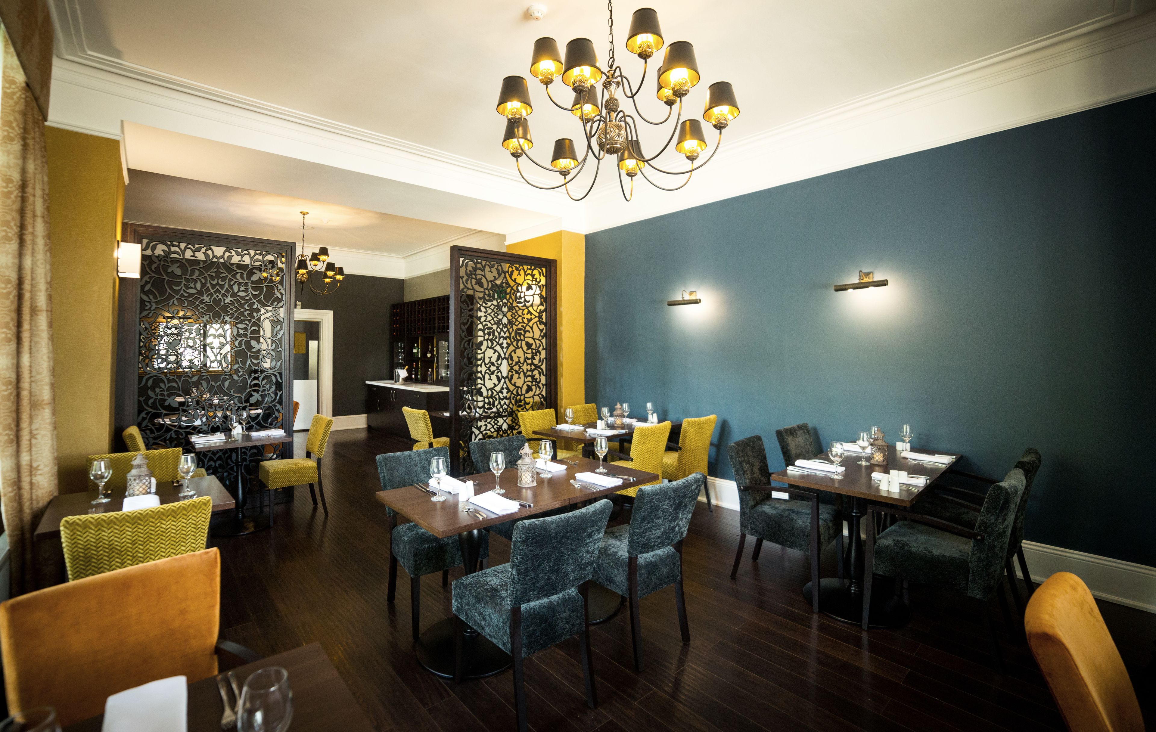 A dining area with multiple tables and chairs, a chandelier, and decorative wall panels.