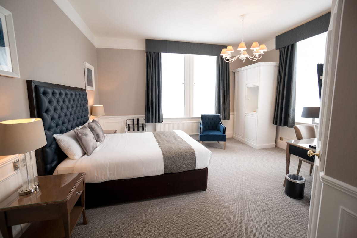 Ein Hotelzimmer mit einem großen Bett, einem Schreibtisch, einem Sessel und einer Chandelier.