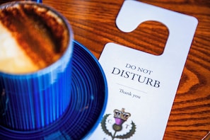 Una taza azul con un platillo y una tarjeta blanca con el texto 'DO NOT DISTURB Thank you' y un escudo.