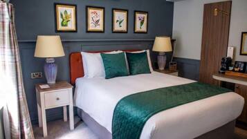 A neatly made bed with a green blanket, two bedside tables with lamps, a wall-mounted air conditioner, and framed floral artwork.