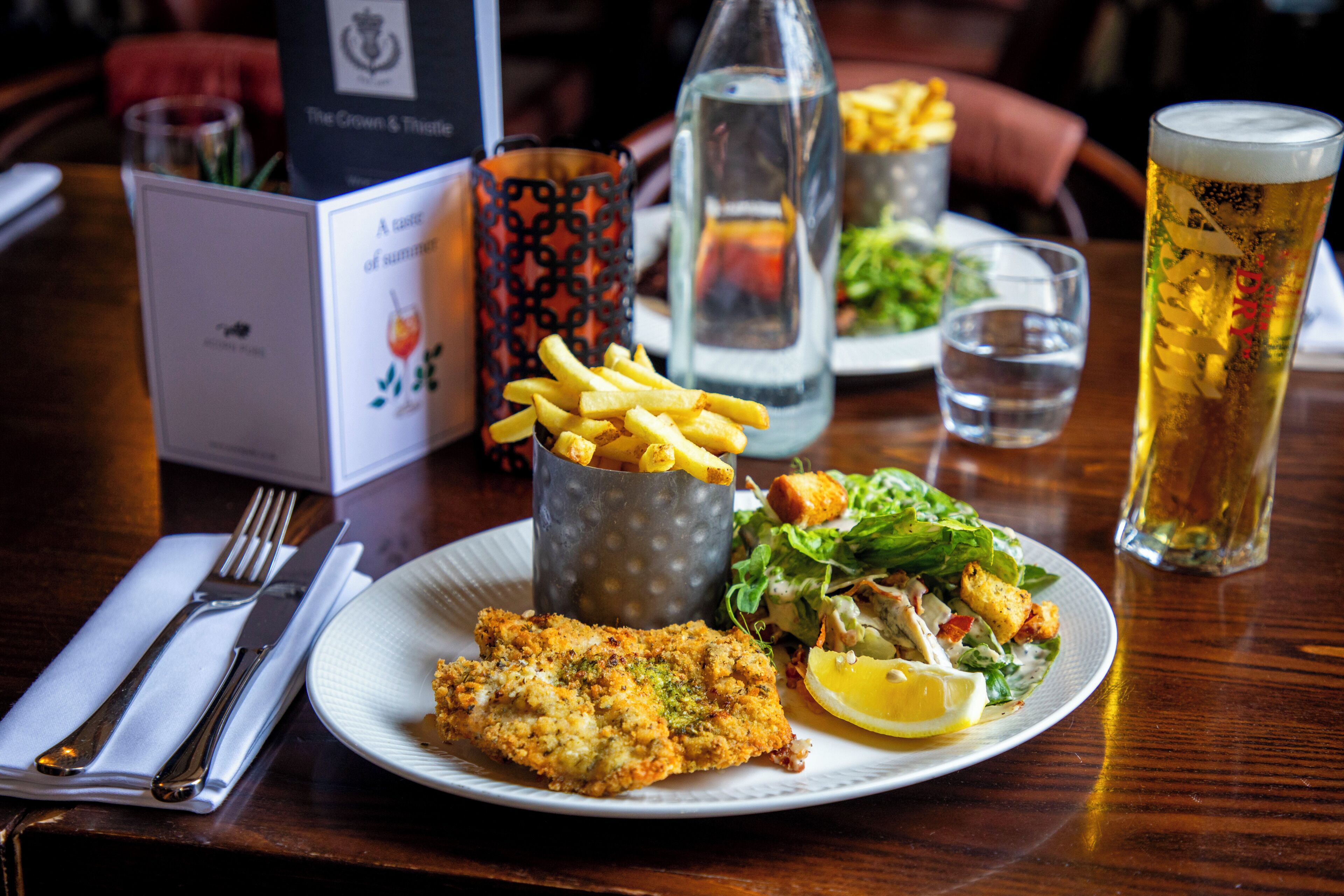 A meal consisting of a breaded fish fillet, a side salad, and French fries, served on a white plate with a lemon wedge.