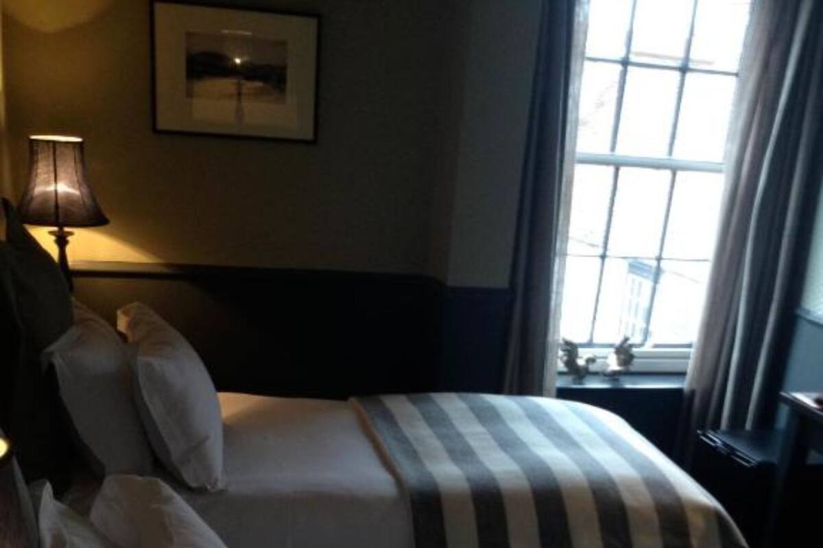 Une chambre d’hôtel avec deux lits, une lampe, un tableau encadré au mur et une fenêtre avec des rideaux.