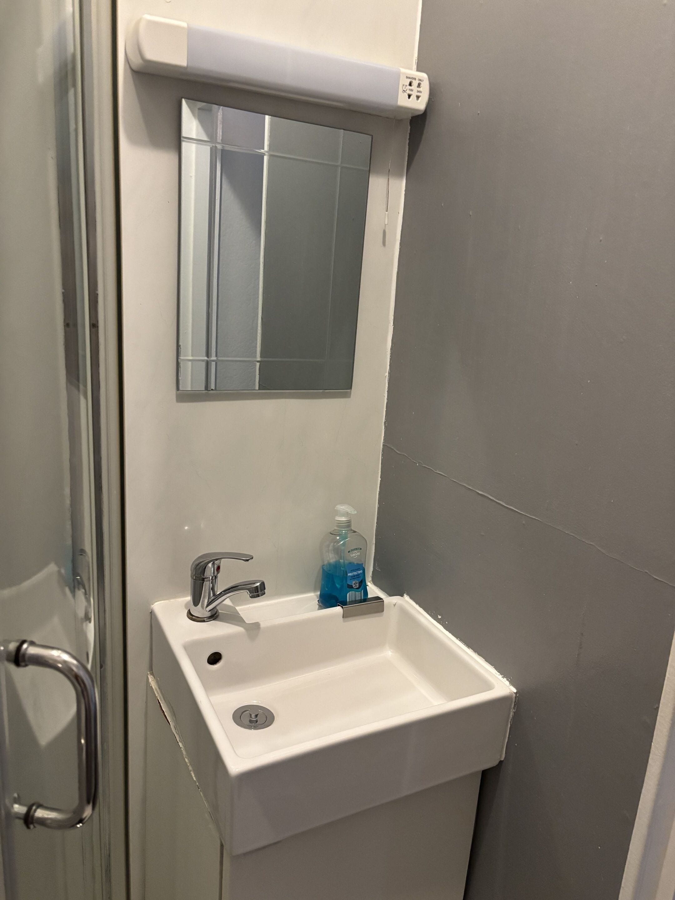 A bathroom with a white sink, a mirror, and a soap dispenser.