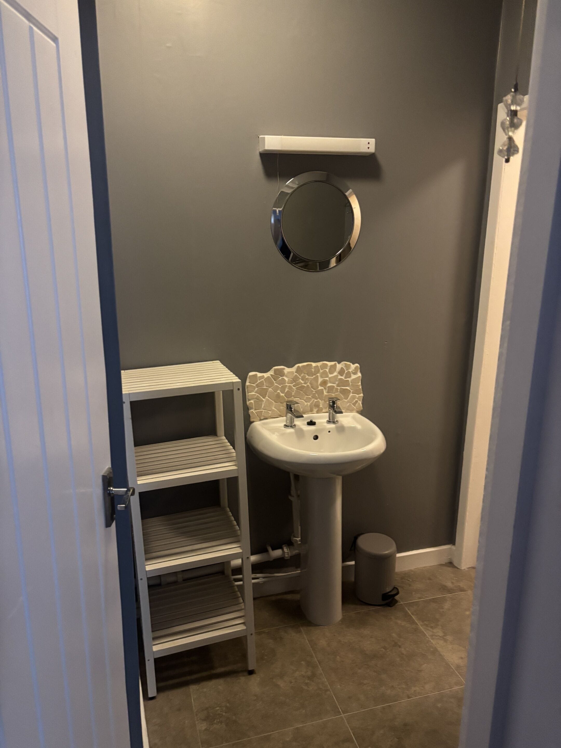 Une salle de bain avec un lavabo blanc, un miroir et un sol carrelé.