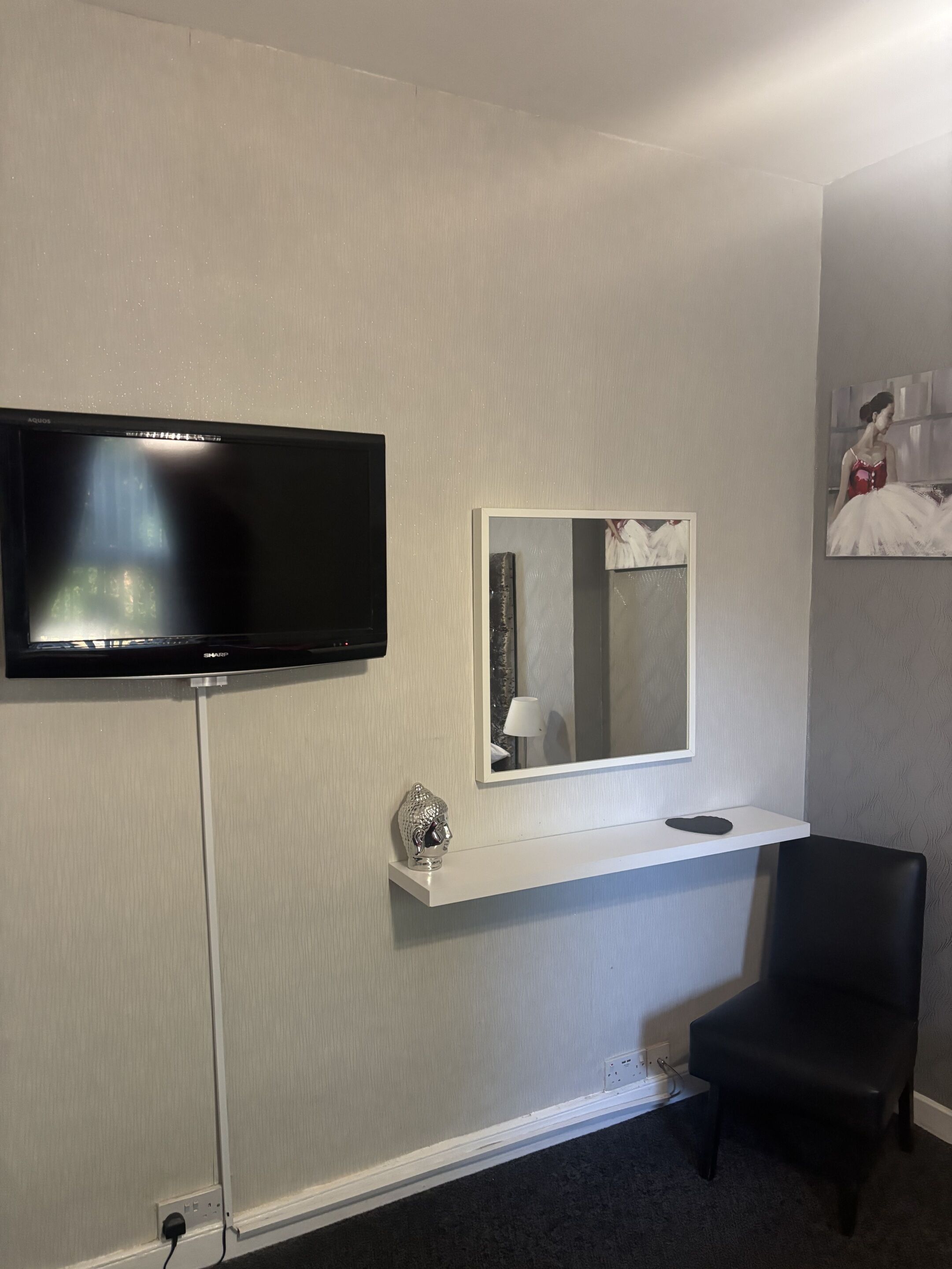 Une chambre d’hôtel dotée d’un téléviseur à écran plat fixé au mur, d’une petite console blanche surmontée d’un miroir et d’une chaise noire.