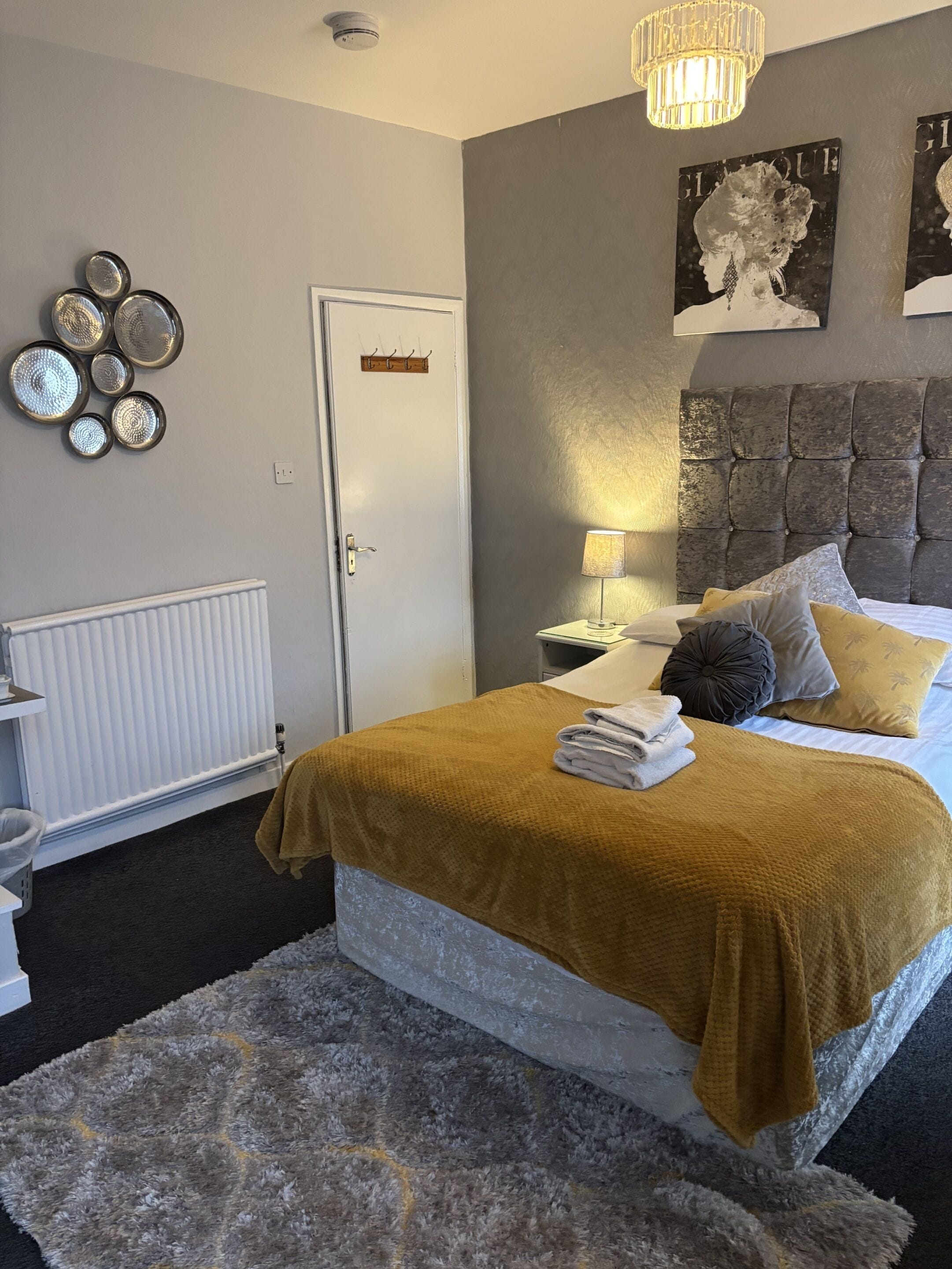 Ein Schlafzimmer mit Bett, Nachttisch, Lampe, Heizkörper und Wanddekorationen.