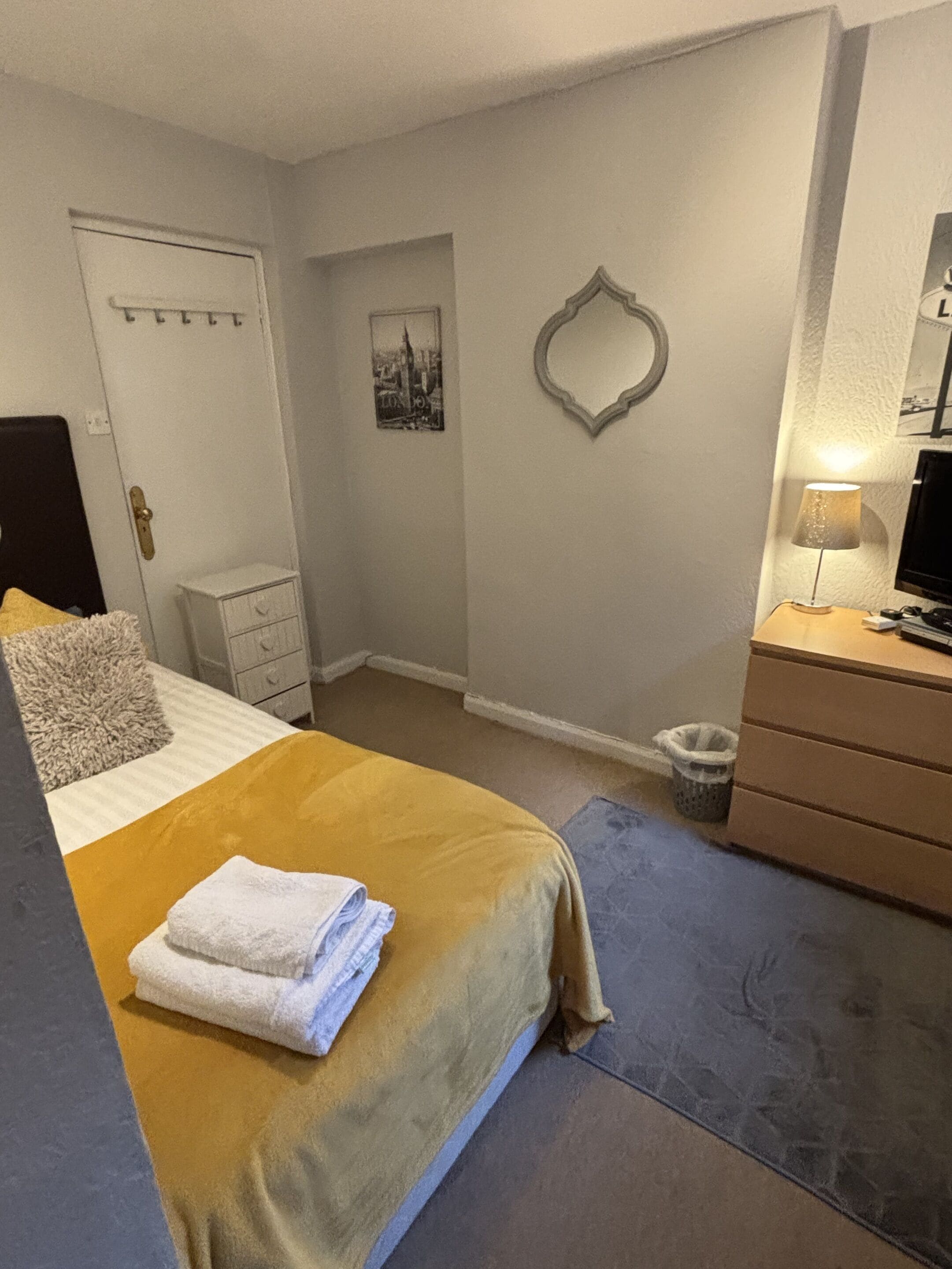 Un dormitorio con cama, cómoda, espejo, lámpara y puerta.