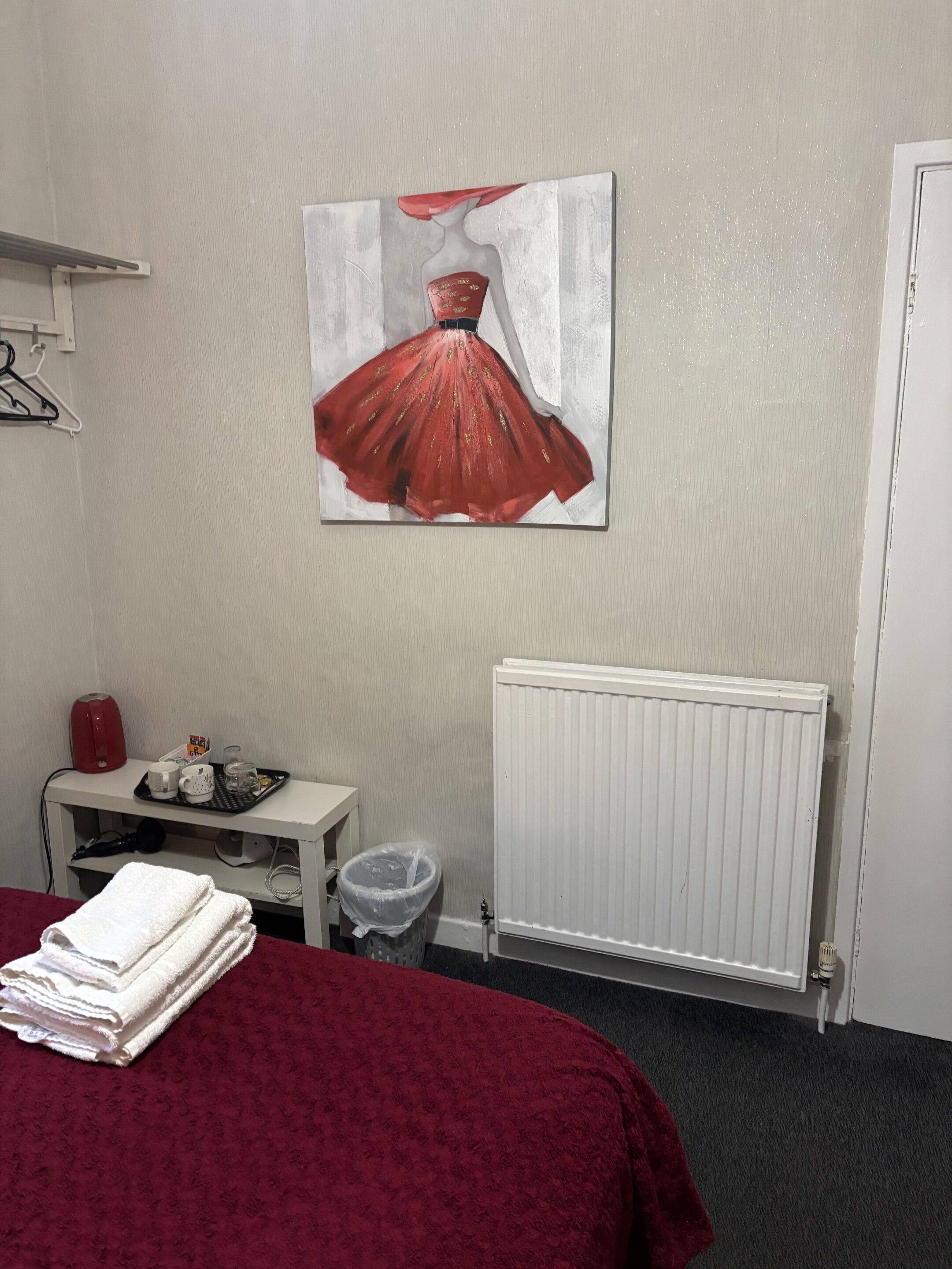 Ein Hotelzimmer mit Bett, Heizkörper, einem kleinen Tisch mit Tablett und einem Mülleimer.