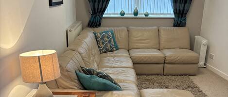A living room with a beige sofa, a wooden side table with a lamp, a small rug, and a radiator.
