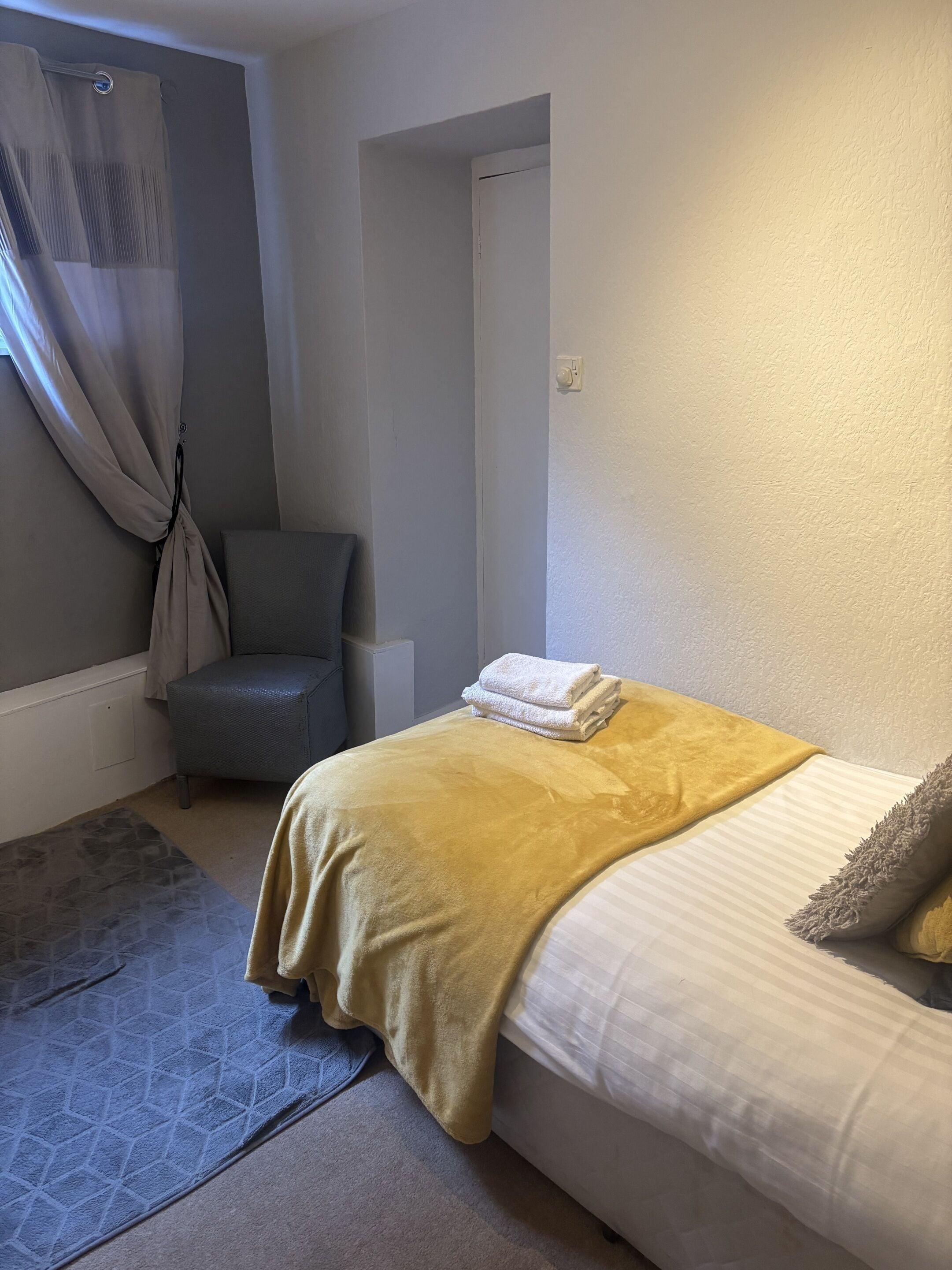 Een slaapkamer met een bed, een stoel, een raam met gordijnen en een deur.