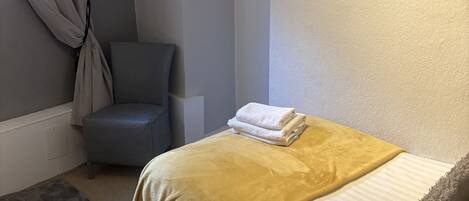 Een slaapkamer met een bed, een stoel, een raam met gordijnen en een deur.