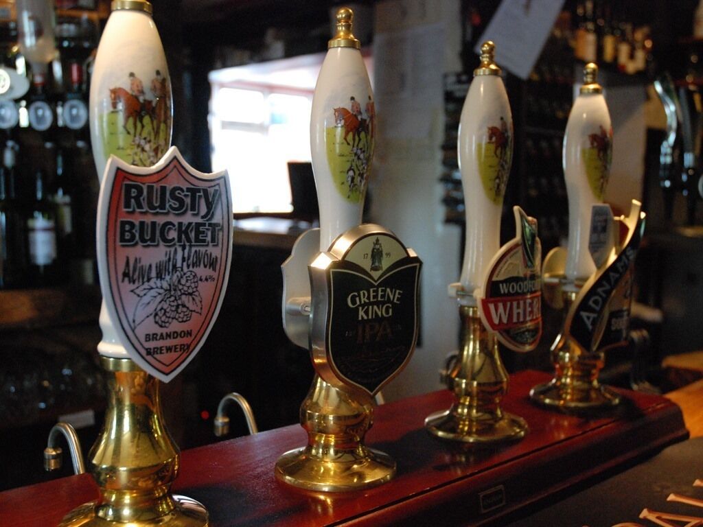 A bar with multiple beer taps, including brands like Rusty Bucket and Greene King IPA.