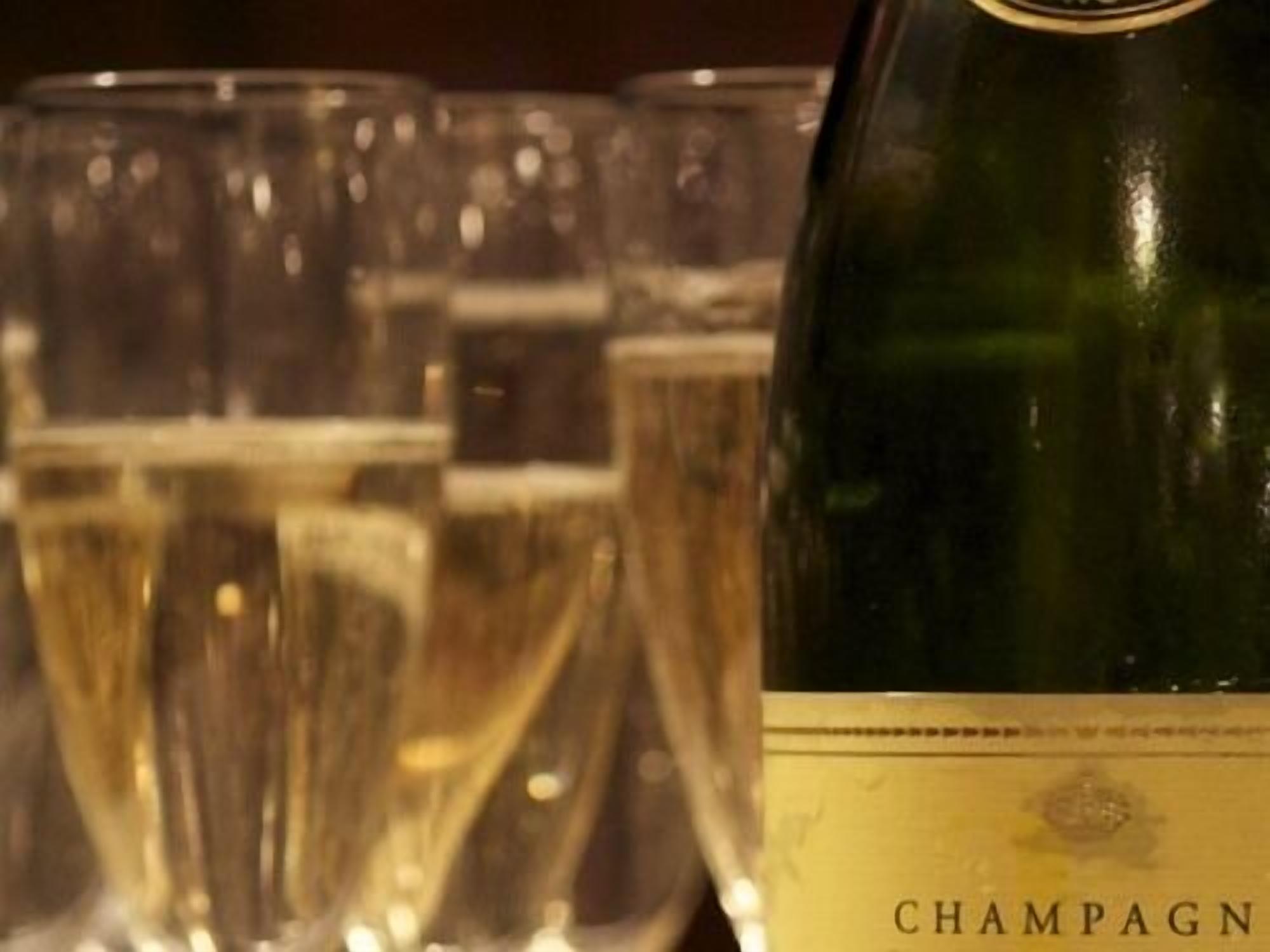 Une bouteille de champagne dont l’étiquette porte l’inscription « CHAMPAGNE », et plusieurs verres remplis de champagne en arrière-plan.