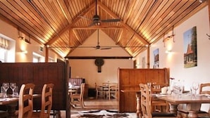A rustic dining area with wooden tables and chairs, a high wooden ceiling, and a cowhide rug on the floor.