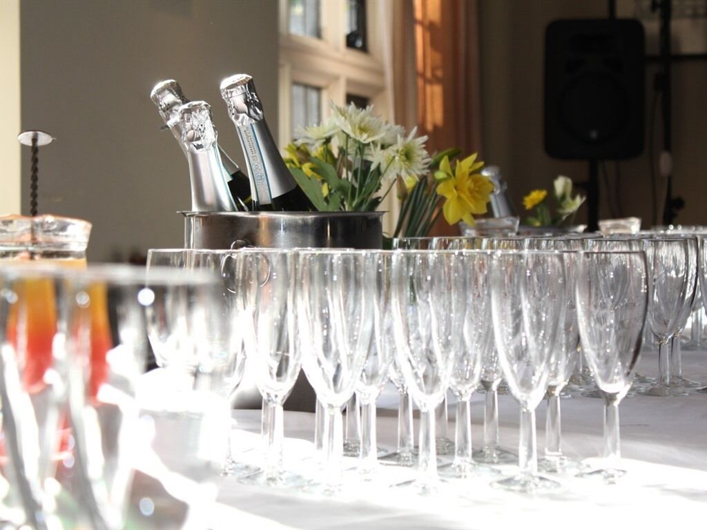 Una mesa con copas de champán y un balde de botellas de champán, con un ramo de flores al fondo.