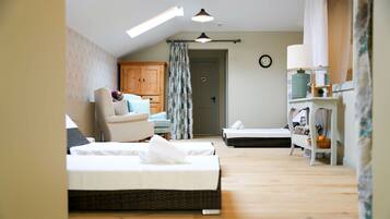 A bedroom with two beds, a wooden wardrobe, a chair, a small table with a lamp, and a window with a curtain.