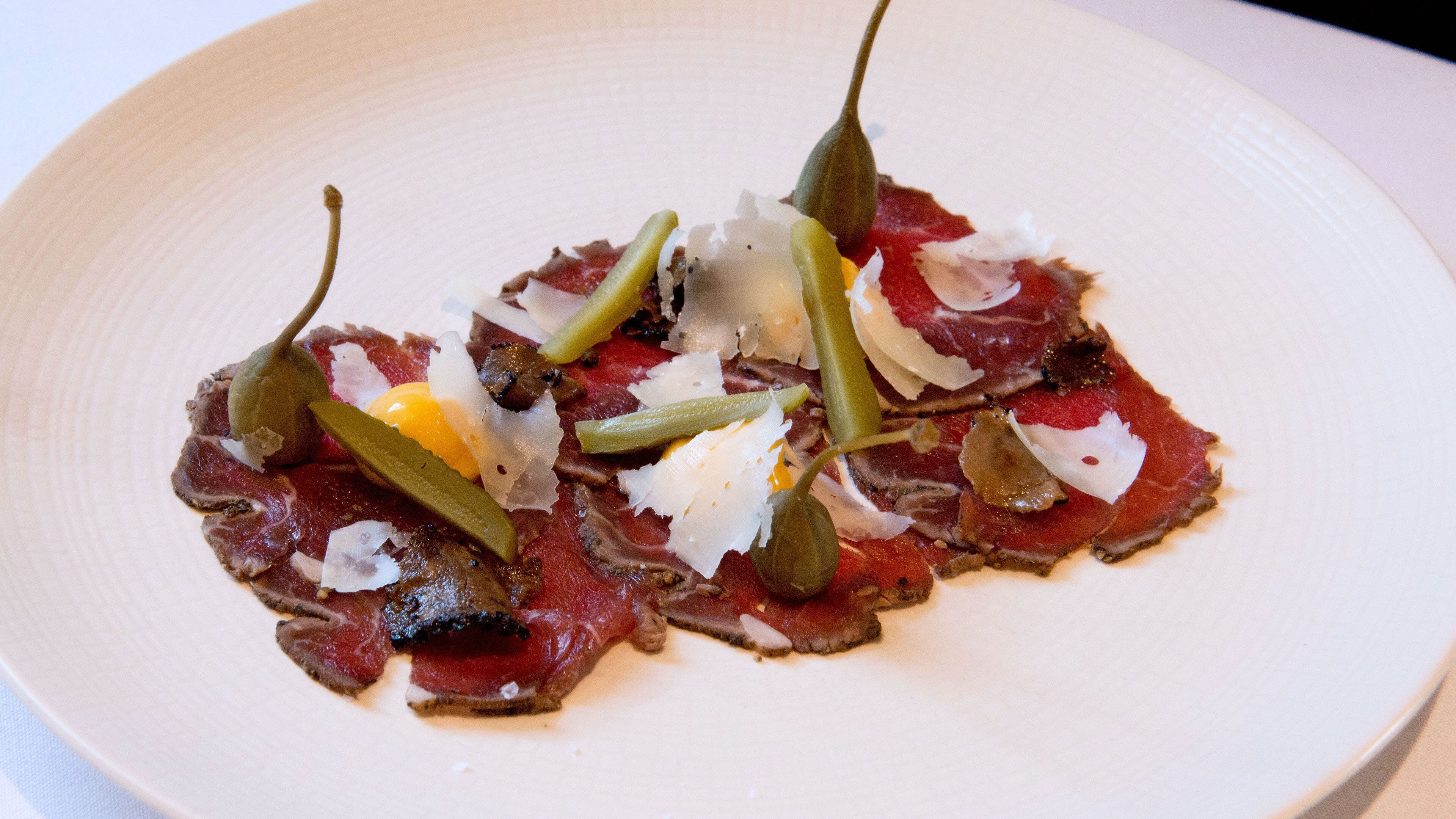 Une assiette de viande coupée en fines tranches, accompagnée de cornichons et de fromage.