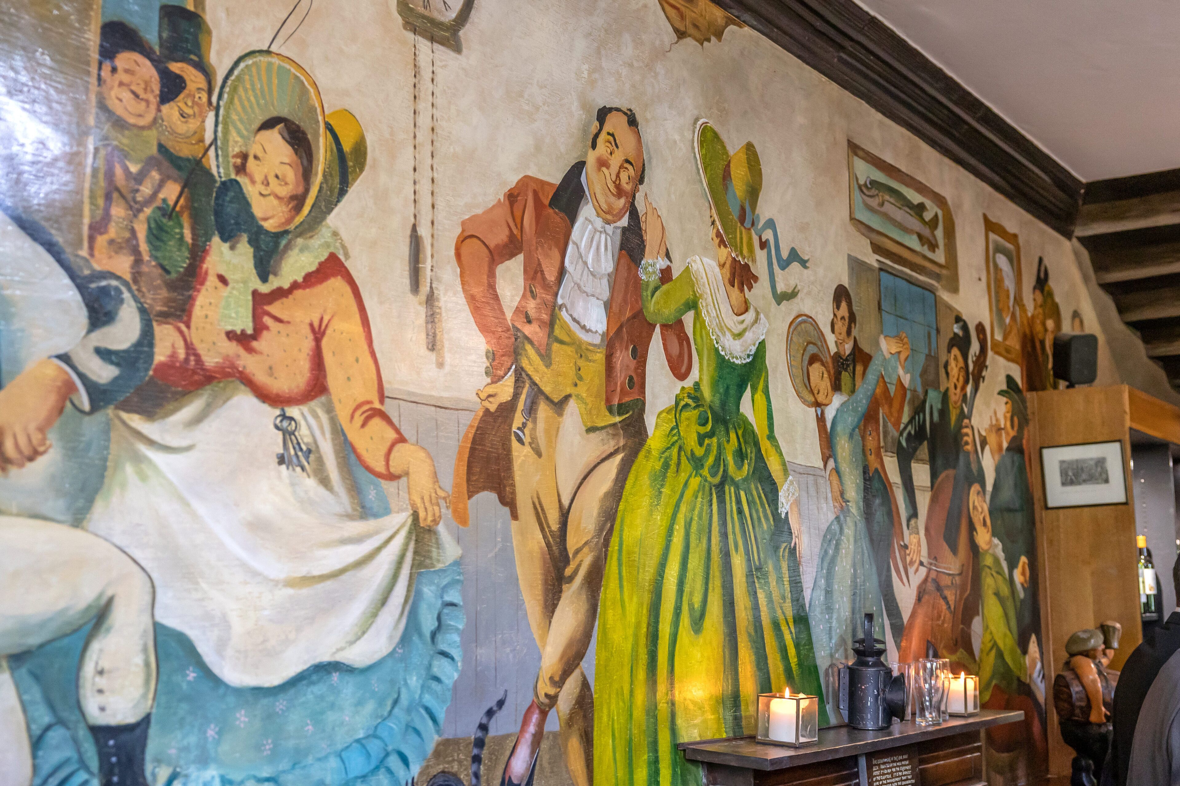 A mural with various figures and a table with candles.