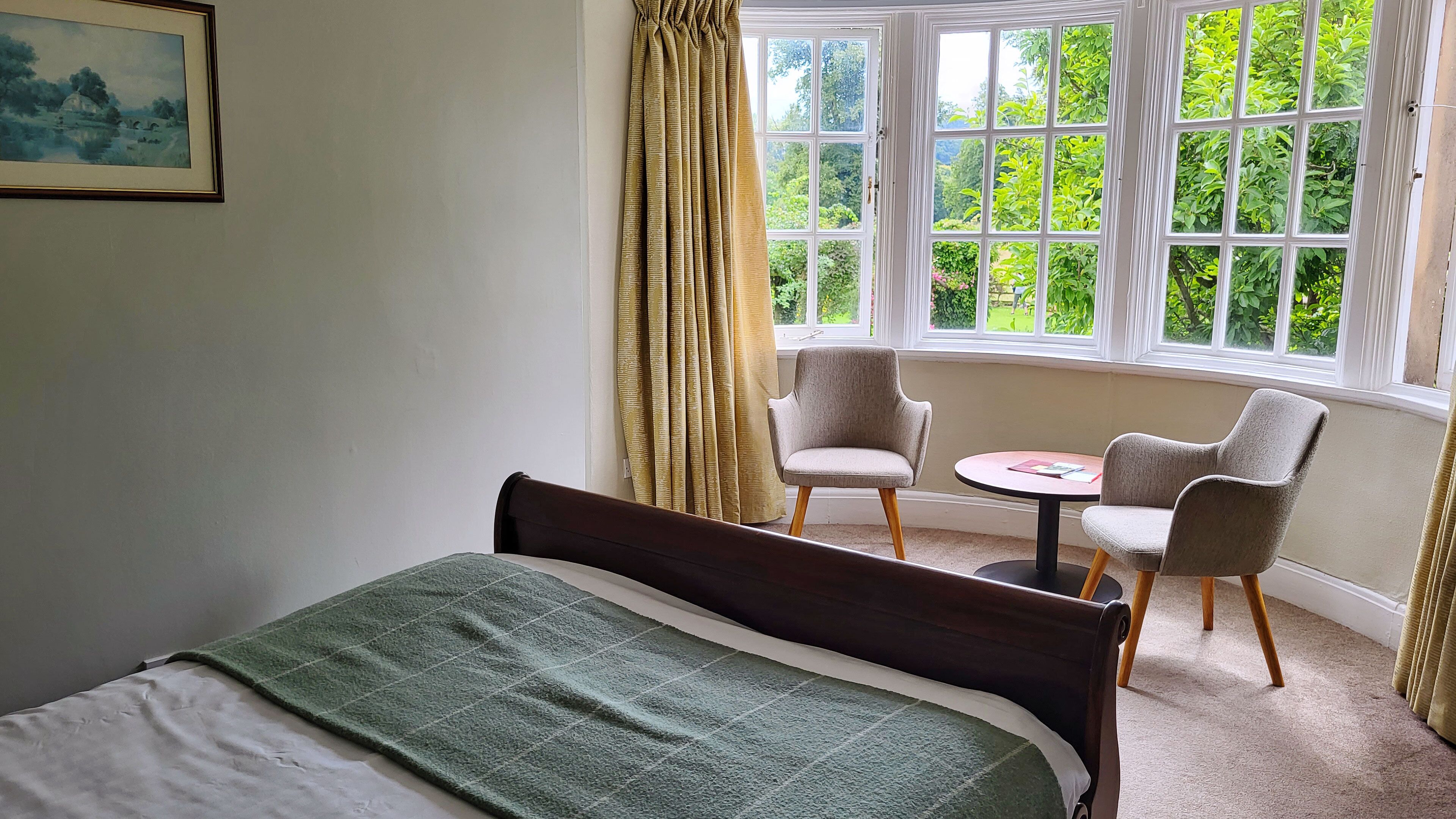 Un dormitorio con una cama, dos sillas, una mesita y una ventana con cortinas.