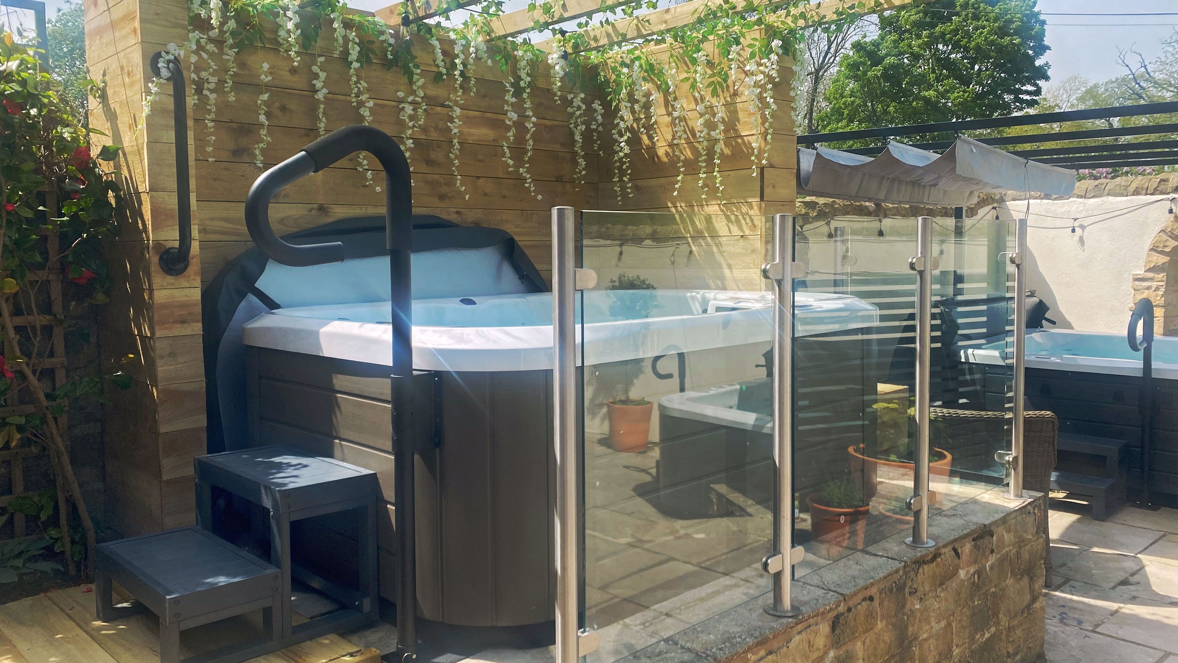 A hot tub with a glass enclosure, surrounded by potted plants and a wooden pergola.