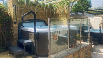 A hot tub with a glass enclosure, surrounded by potted plants and a wooden pergola.