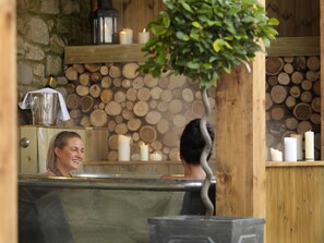 Ein Wellnessbereich mit Steinwand, Holzstämmen und Kerzen.