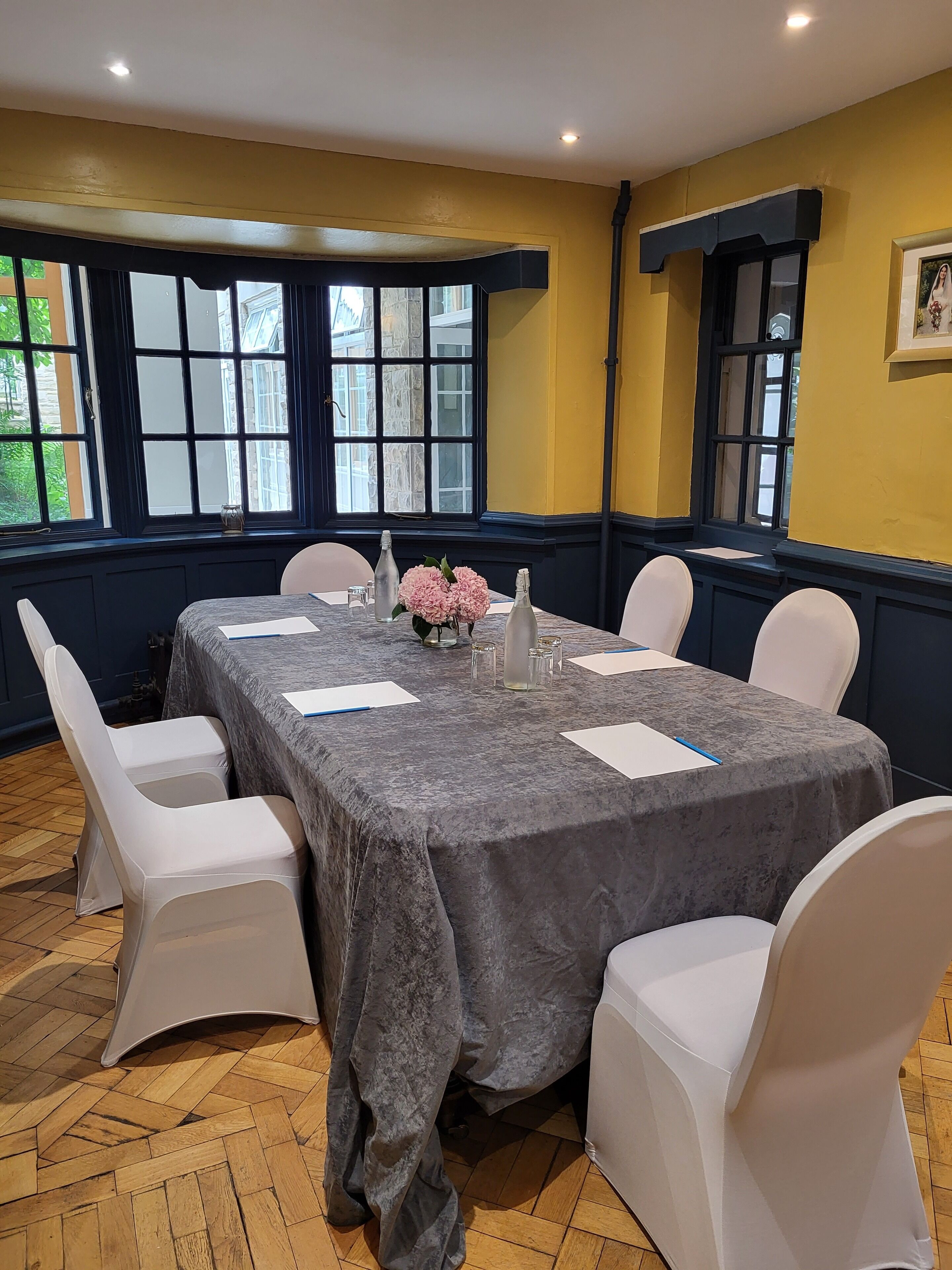 A conference room with a large table, white chairs, and a vase of flowers.