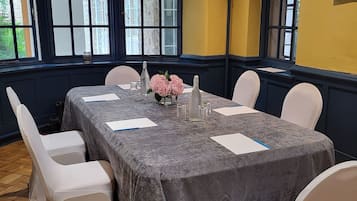 A conference room with a large table, white chairs, and a vase of flowers.