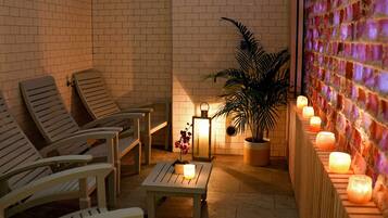 A cozy outdoor seating area with wooden chairs and a table, a potted plant, and wall-mounted candles providing ambient lighting.