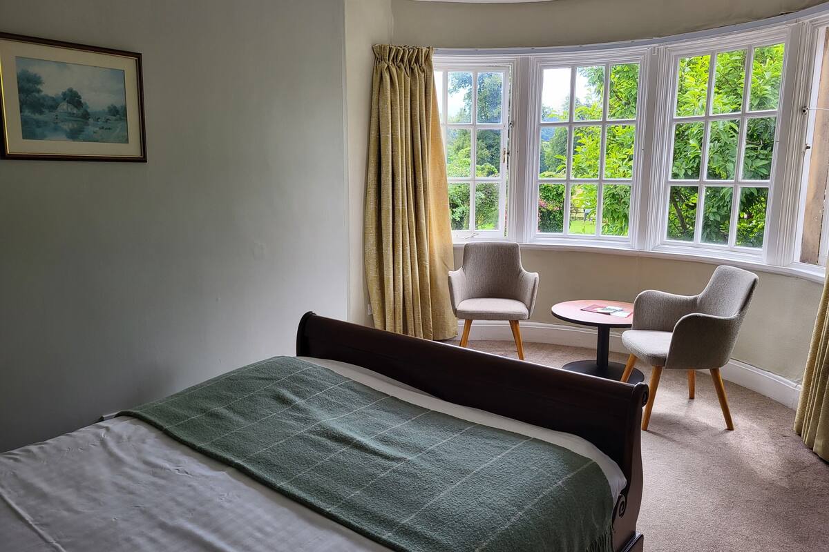 A bedroom with a bed, a small round table, two chairs, and a window with curtains.