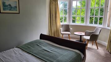 Un dormitorio con cama, una mesita redonda pequeña, dos sillas y una ventana con cortinas.