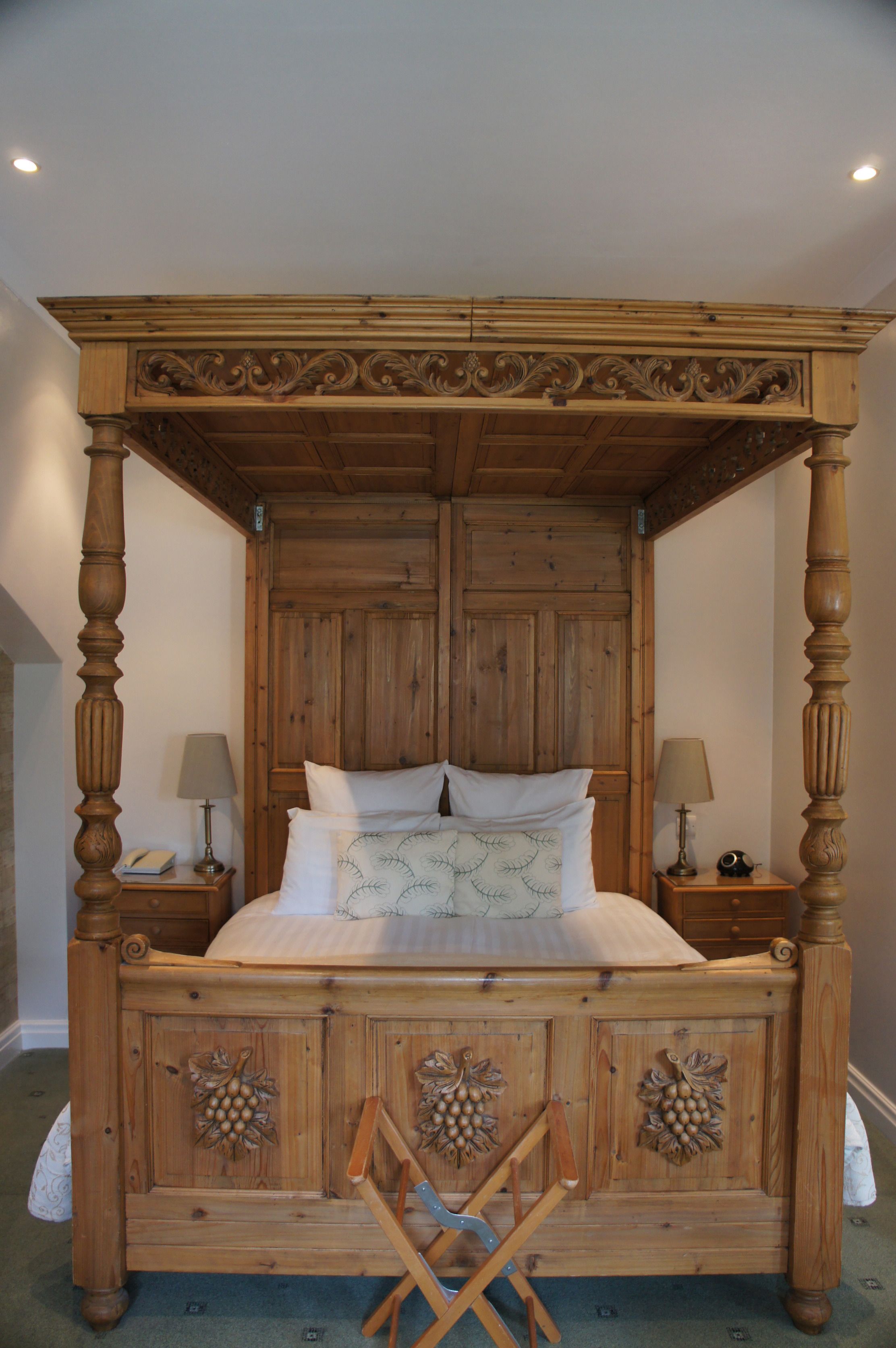 Una cama con dosel de madera, dos mesitas de noche y una silla plegable.