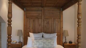 Una cama con dosel de madera, dos mesitas de noche y una silla plegable.