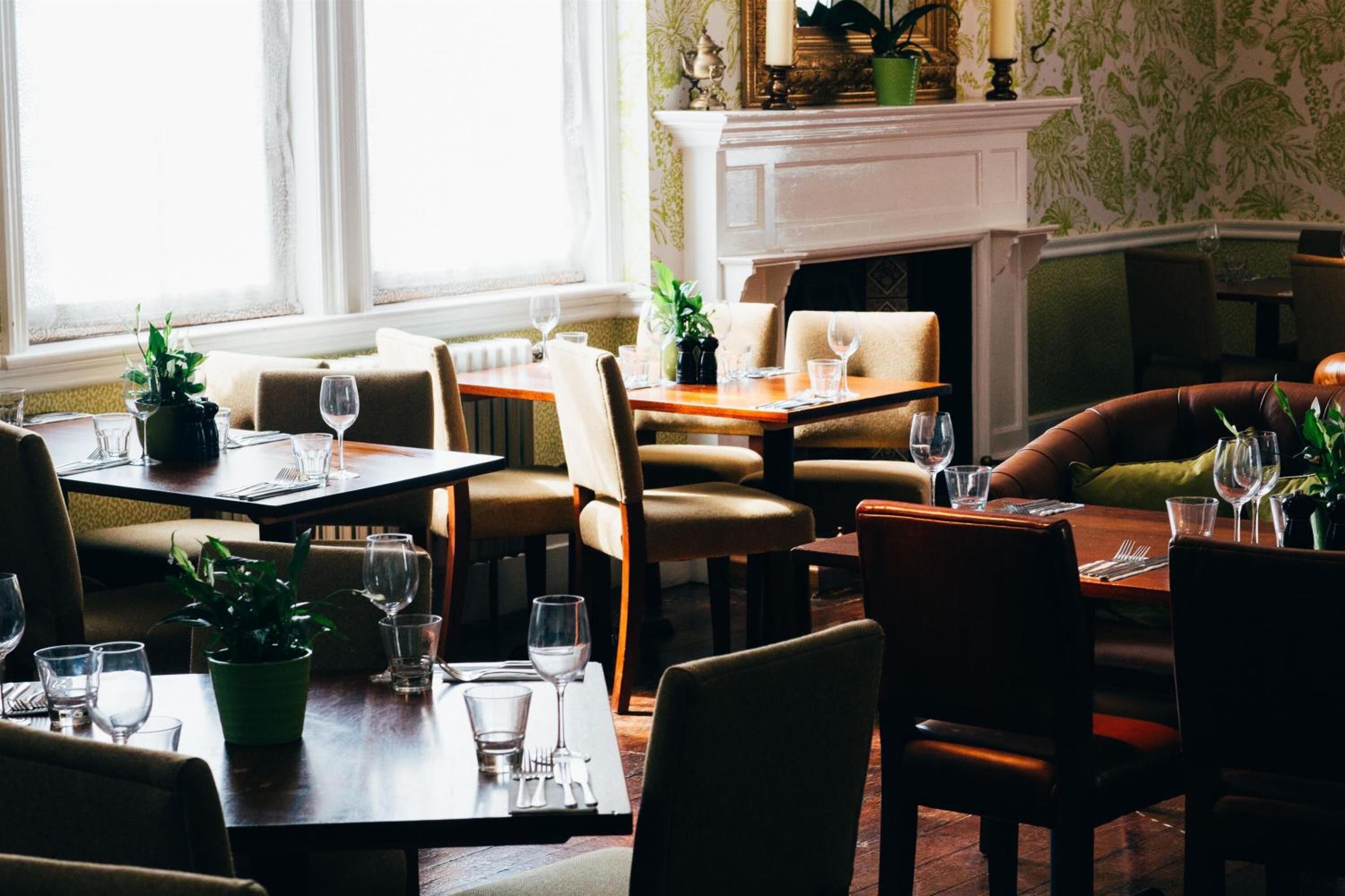 A dining area with tables set for four, chairs, and potted plants.