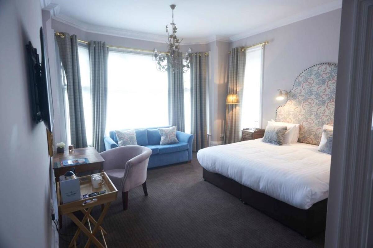 A hotel room with a bed, a desk with a chair, a sofa, and a chandelier.