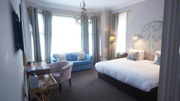 A hotel room with a bed, a desk with a chair, a sofa, and a chandelier.