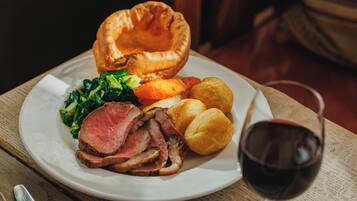 A plate of food including roast beef, Yorkshire pudding, vegetables, and a glass of red wine.