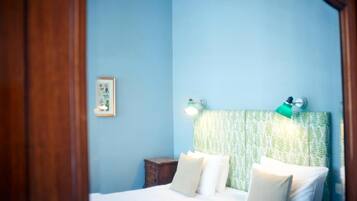 Un dormitorio con cama, almohadas, una mesita de noche, un cuadro enmarcado y lámparas fijadas a la pared.