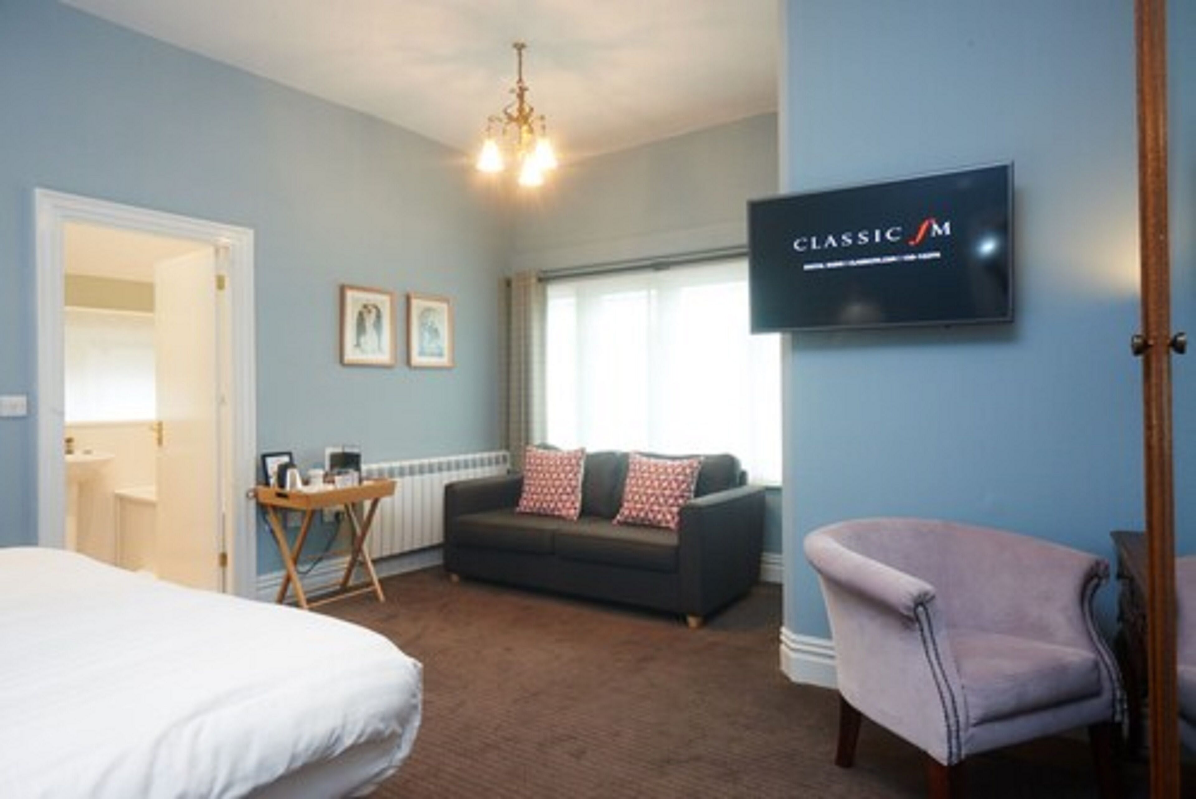 A hotel room with a bed, a sofa, a chair, a TV, and a window with curtains.