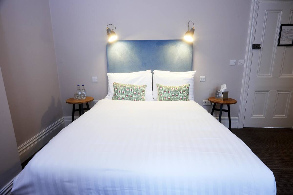 A hotel room with a large bed, two bedside tables, and a headboard with wall-mounted lights.