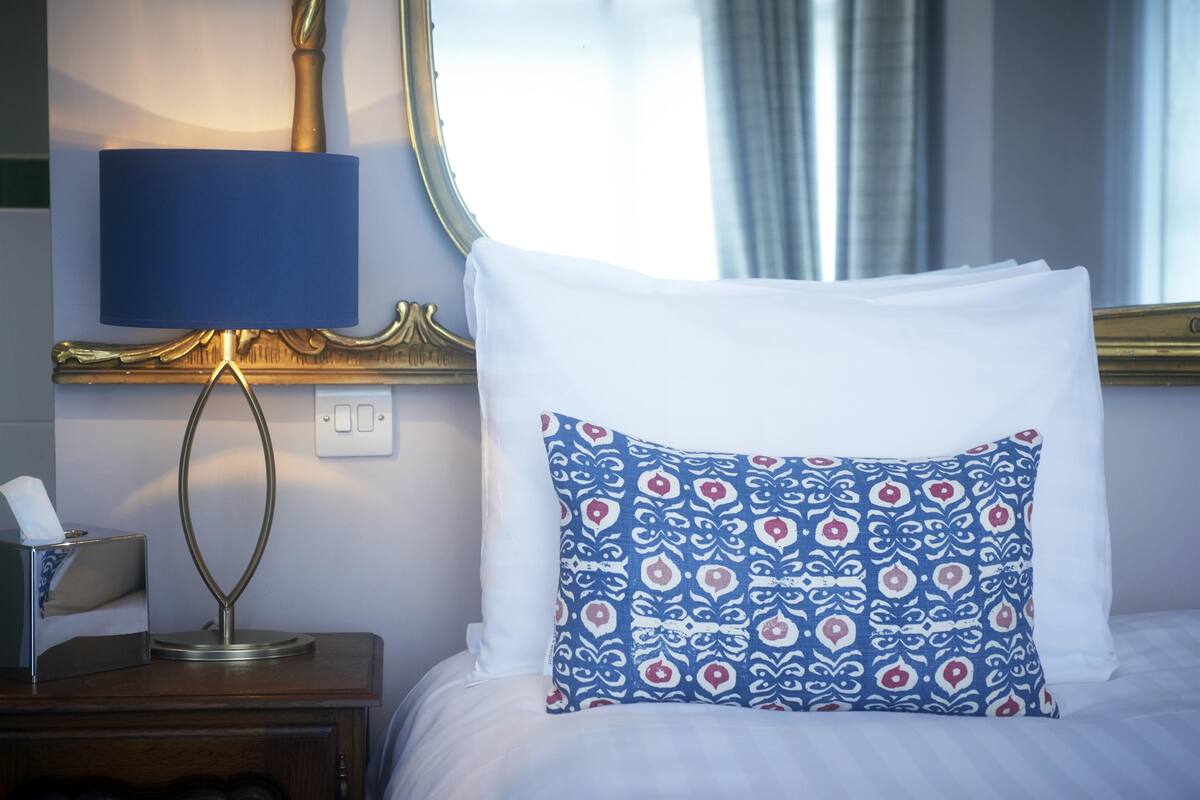 A neatly made bed with a patterned pillow, a bedside lamp, and a tissue box on a wooden nightstand.