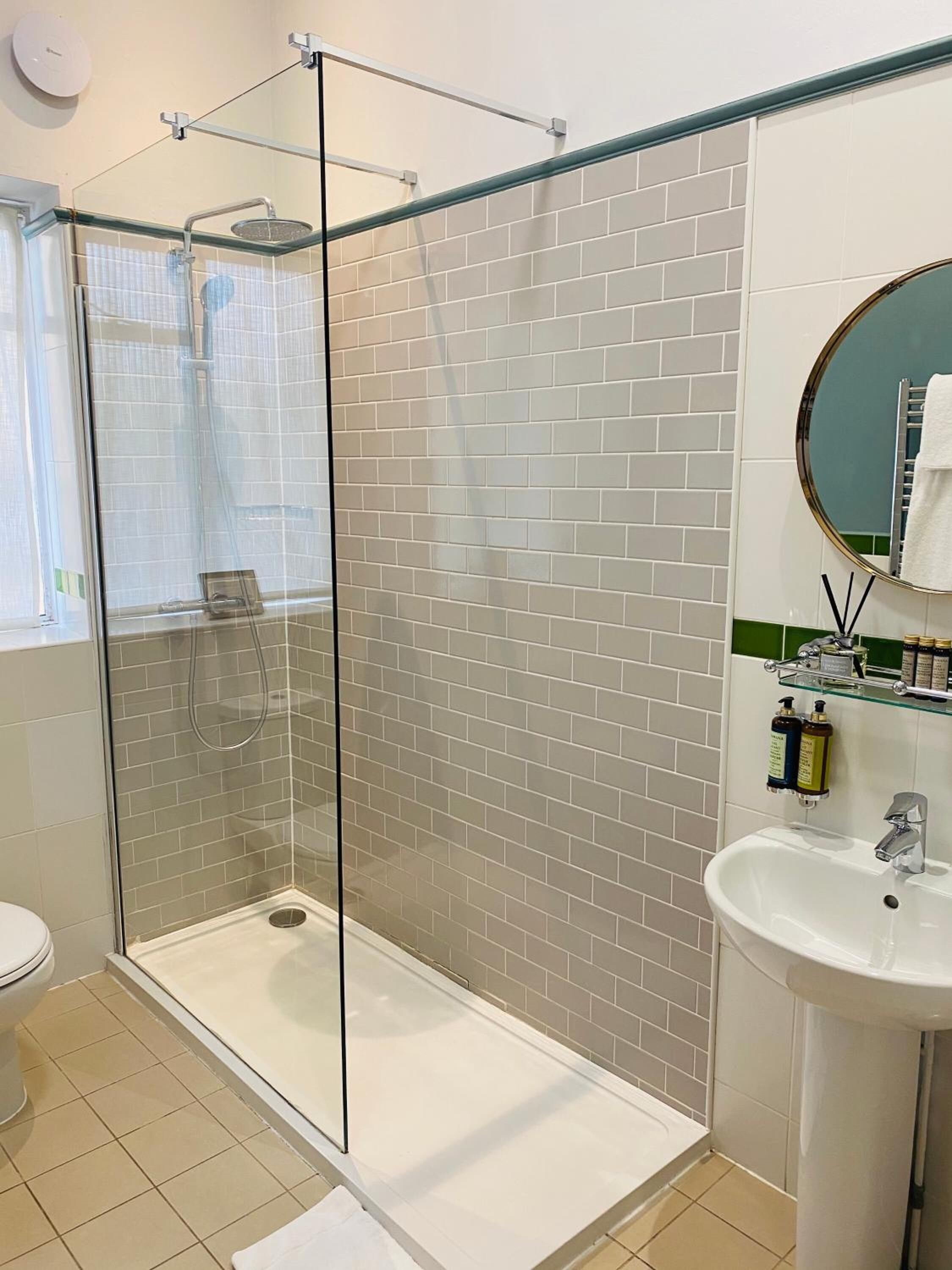 A modern bathroom with a glass-enclosed shower, white tiled walls, a white sink, and a round mirror.