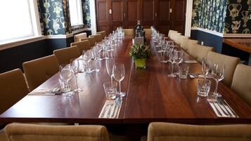 A long conference table set for a meeting with chairs around it, a small plant in the center, and a window with patterned curtains.