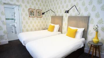 Une chambre d’hôtel avec deux lits, une salle de bain visible à travers une porte ouverte et une petite table sur laquelle se trouve un vase.
