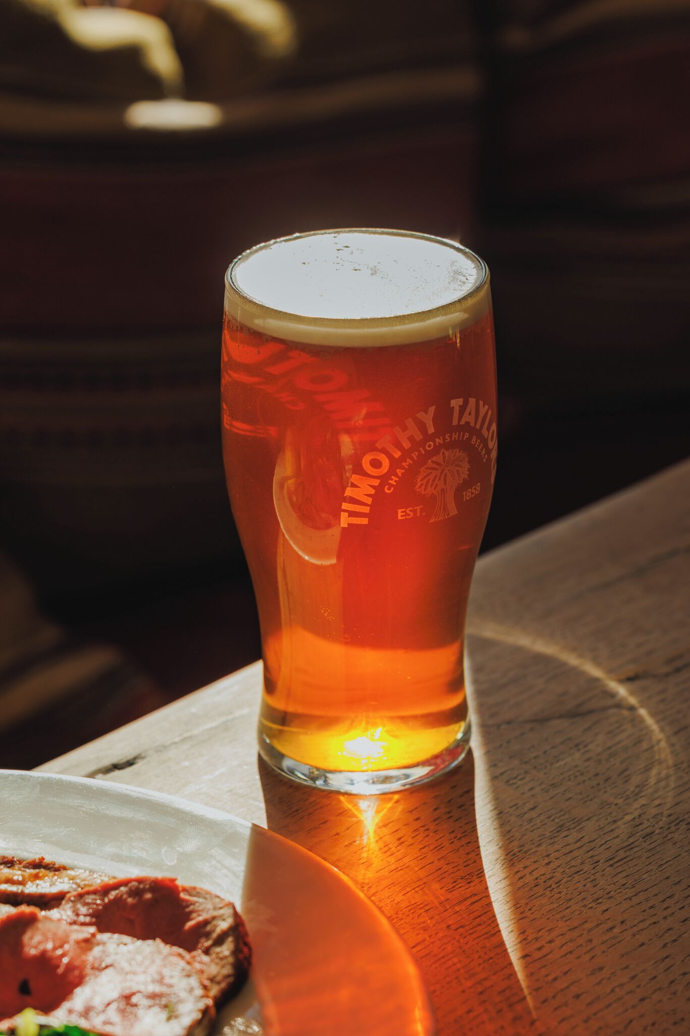 Un verre de bière sur une table en bois, avec une serviette et une assiette de nourriture.