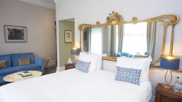 A hotel room with a large bed, a blue sofa, a small round table, and a large mirror.