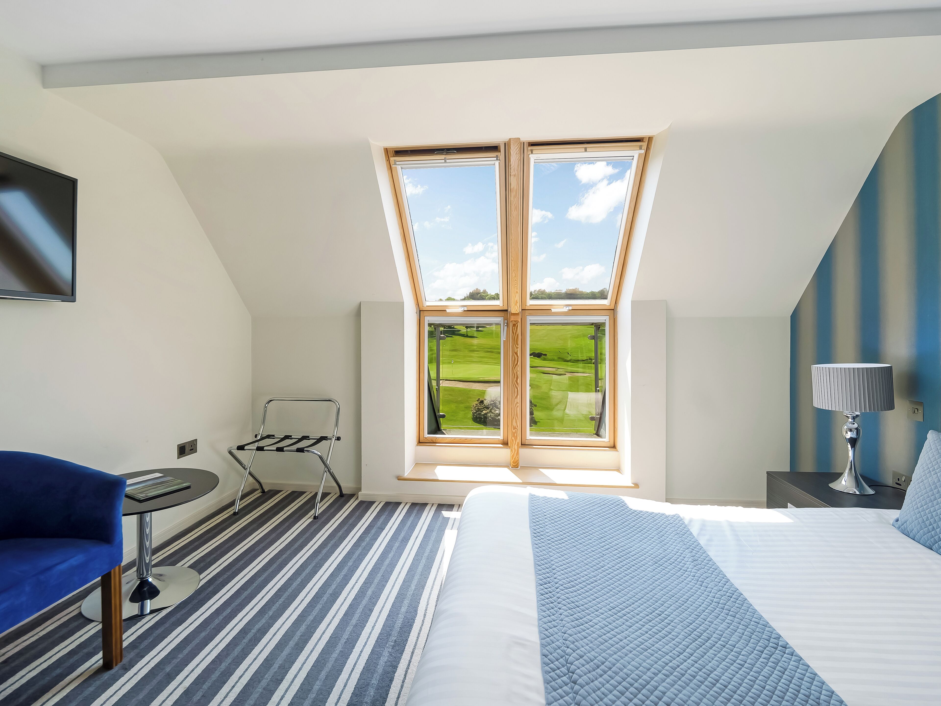 Une chambre avec un puits de lumière, un lit, une chaise, une table et une lampe.