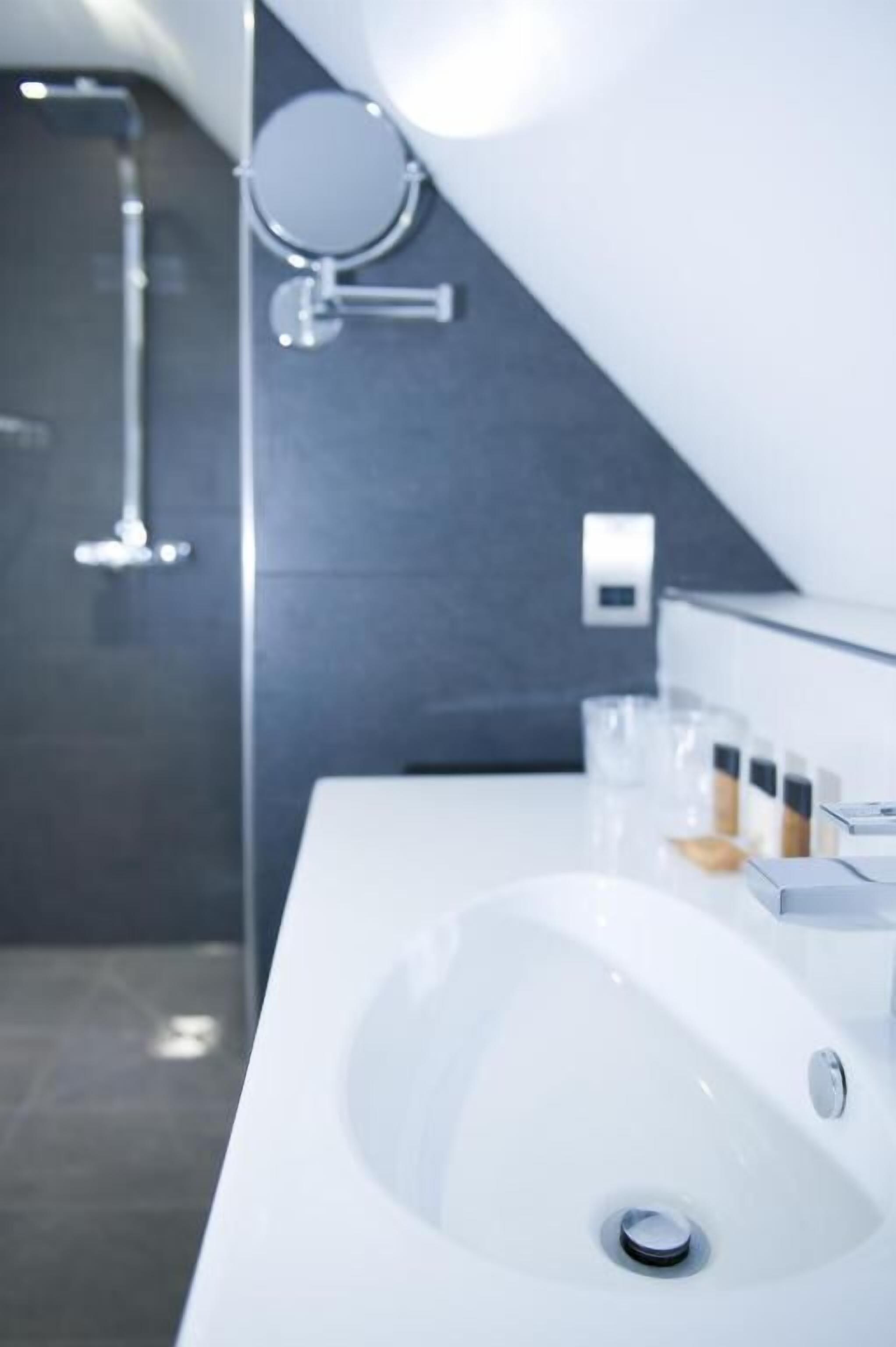 Un baño moderno con un lavamanos blanco, un espejo y una zona de ducha.