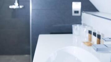 Un baño moderno con un lavamanos blanco, un espejo y una zona de ducha.